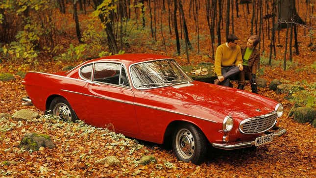A photo of a red Volvo P1800 coupe in the woods. 