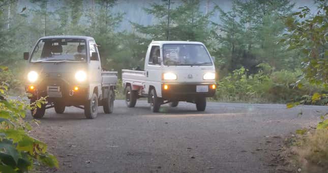 A Suzuki Carry and Honda Acty pickups are parked with headlights on in a forest