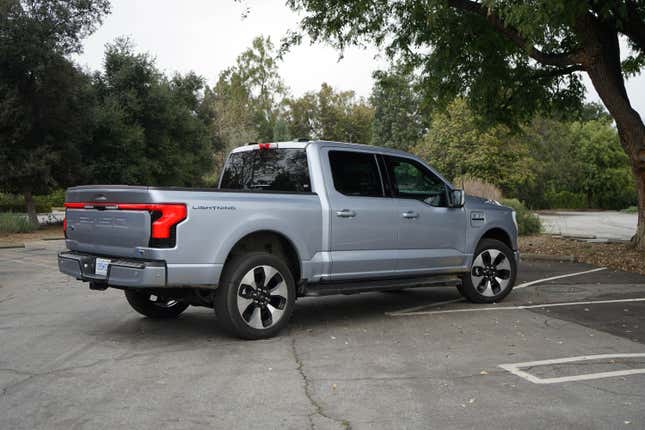A silver 2023 Ford F-150 Lightining is parked in rear-three-quarter view in front of some trees