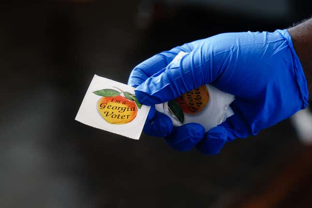 ATLANTA, GA - JUNE 09: A polling place worker holds an “I’m a Georgia Voter” sticker to hand to a voter on June 9, 2020, in Atlanta, Georgia. Georgia, West Virginia, South Carolina, North Dakota, and Nevada are holding primaries amid the coronavirus pandemic.