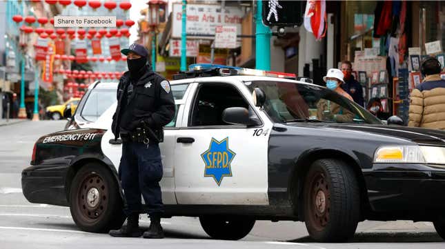 An SFPD officer with his face covered stands in front of a SFPD cruisers in Chinatown. 