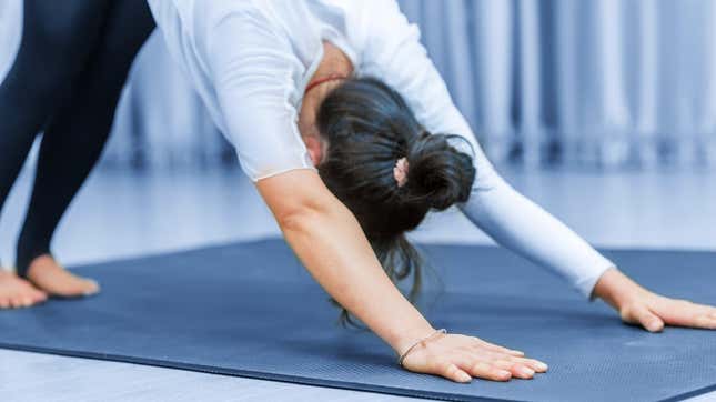 A woman doing a downward dog yoga post over a blue yoga mat