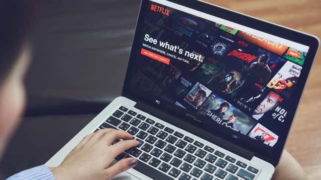 A person with a macbook laptop stares at the main Netflix splash screen with their hands hovering over the keyboard.