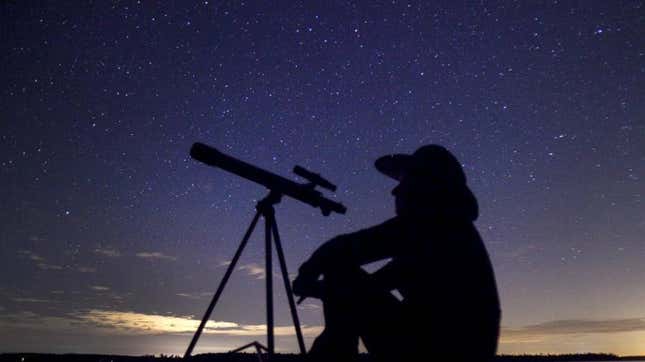 A photo of a man in silhouette with a telescope in front of a starry sky.