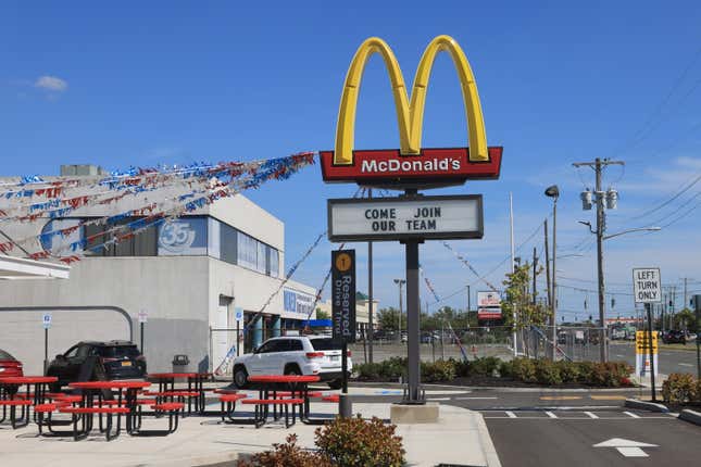A McDonald's golden arches sign that reads "come join our team" underneath. The sign is located in a concrete picnic area.