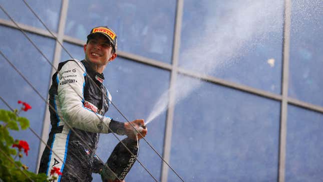 A photo of Esteban Ocon spraying champagne from the podium. 