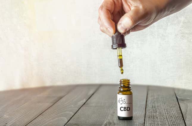 Hand holding pipette with CBD oil on wooden table with copy space