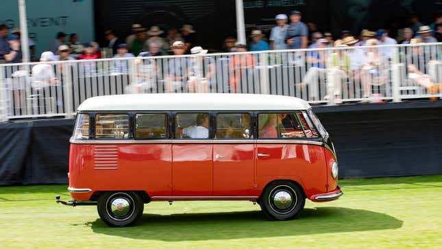 A photo of a red and brown VW bus driving on a field. 