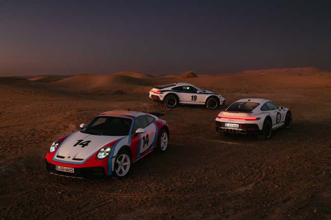 Three Porsche 911 Dakars are parked on sand, each in a different historic rally livery.