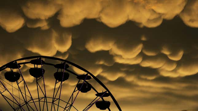 A ferris wheel sits in front of mammatus clouds with the sky illuminated yellow and orange.