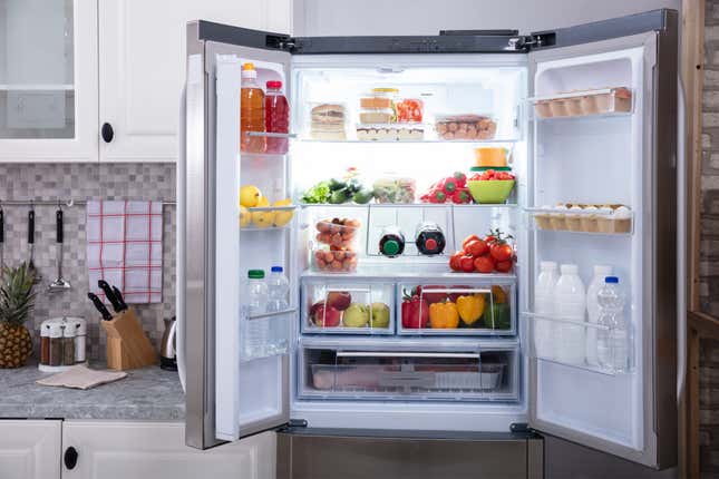 Front-facing photo of an open double-door refrigerator filled with fruits, vegetables, eggs, meats, and dairy products.
