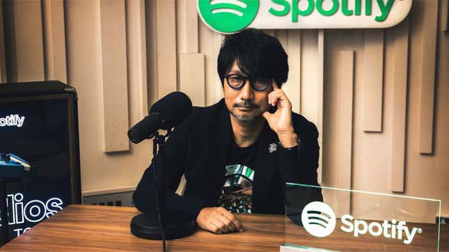 Hideo Kojima sits behind a microphone and looks into the camera at a Spotify studio.