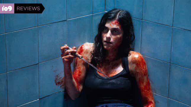 A dark-haired woman with blood smeared on her arms, face, and chest sits in a shower holding a knife in a scene from horror film The Advent Calendar.