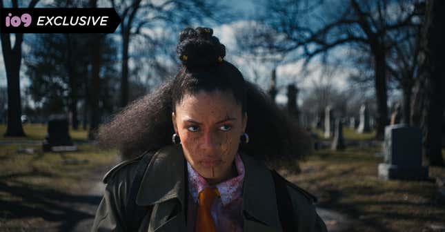 A young woman with blood on her face, looking angry, standing in a graveyard