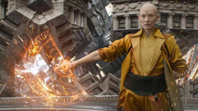 Tilda Swinton's bald Ancient One in yellow robes wielding see-through orange magic in one hand.
