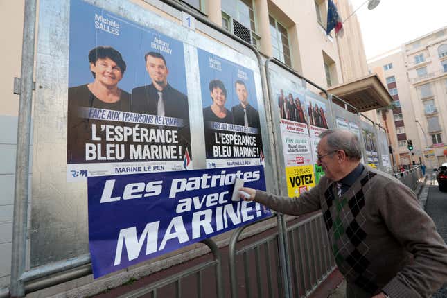 A far-right National Front supporter pastes an electoral poster reading “Patriots with Marine.”