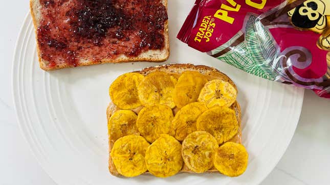 A photo of an unassembled peanut butter and jelly and plantain chips sandwich on a plate. One slice of bread is covered in jelly, the other in peanut butter and plantain chips.