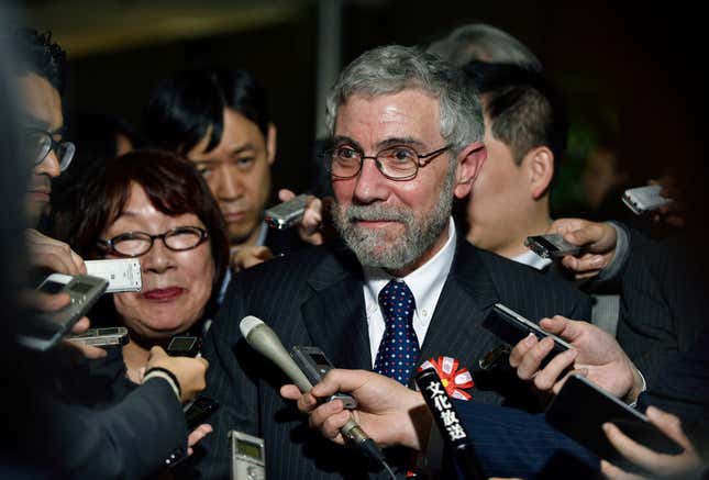 Paul Krugman stands surrounded by microphones and voice recorders.