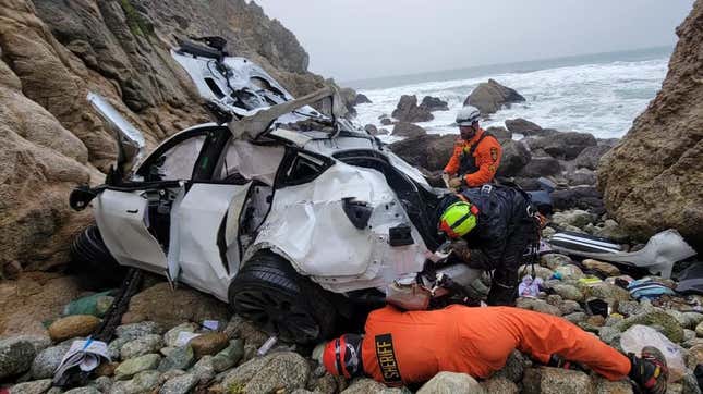 A photo of three rescue workers examining the mangled Tesla at the bottom of a cliff.