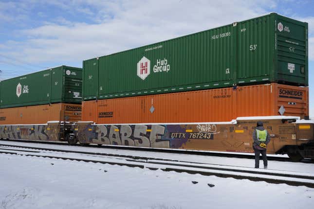 A rail worker in a hi-viz vest watches as a double-decker freight car rolls past.