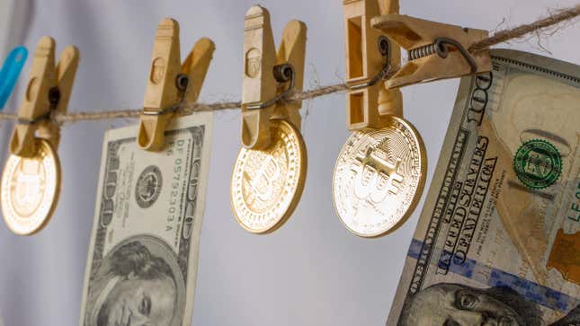 Clothes pins on a string hold up 100 dollar bills alongside crypto coins with the bitcoin symbol.