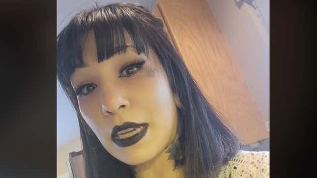 A screenshot of a TikTok in which a young woman with dark shoulder length hair and heavy bangs wearing black lipstick addresses her selfie camera