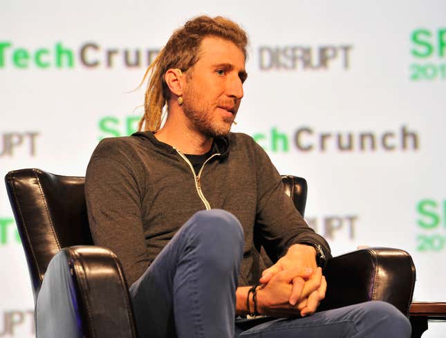 Moxie Marlinspike sitting on a chair in front of signs that say TechCrunch.