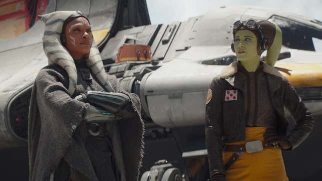 Ahsoka and Hera stand in front of Hera's ship, with Chopper lurking in the background. 