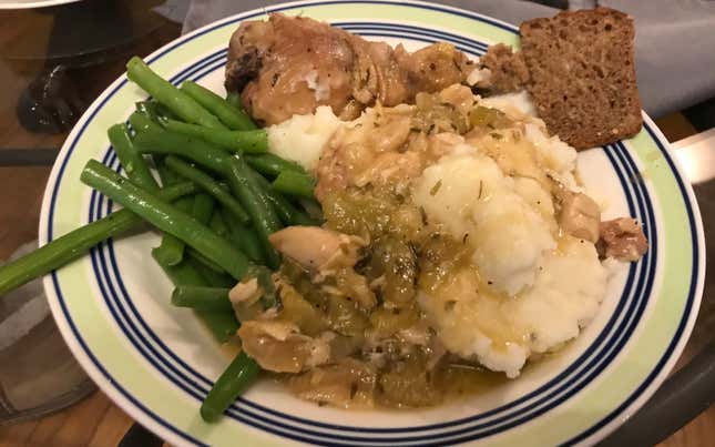 Plate of green beans, mashed potatoes, bread, and chicken, all doused in garlic gloves
