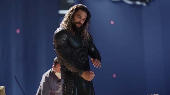 Aquaman (Jason Momoa) in his superhero suit has a stern look on his face while standing on a rocky beach in Lost Kingdom.