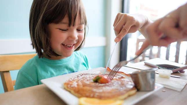 Child smiling as their pancake is sliced by an adult