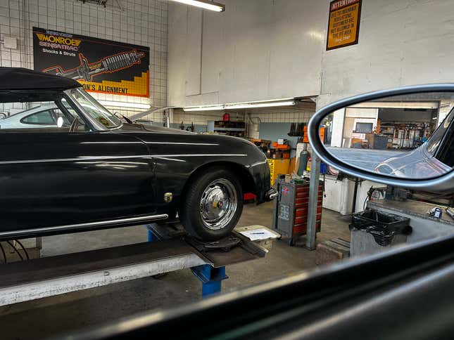 A black Porsche 356 convertible is on an alignment rack.