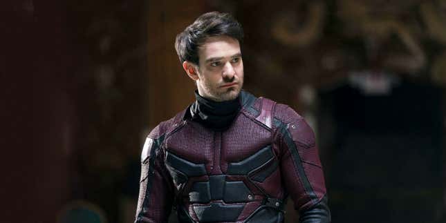 Charlie Cox as Daredevil, wearing the costume, sans mask and looking at a character offscreen.