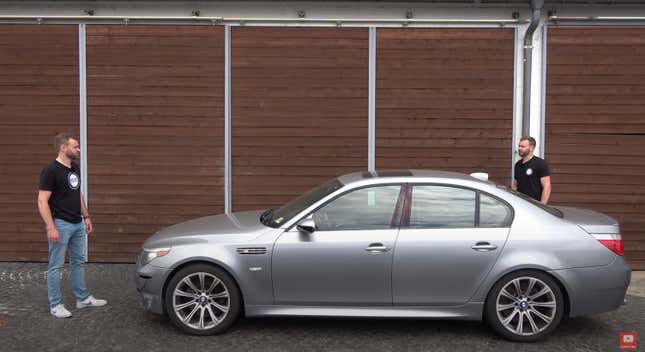 A confused looking man stands staring at his double in front of a BMW E60 M5.