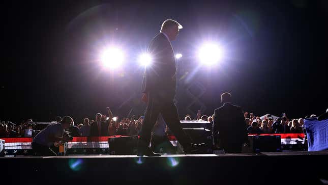 Former U.S. President Donald Trump walks in front of lights on stage.