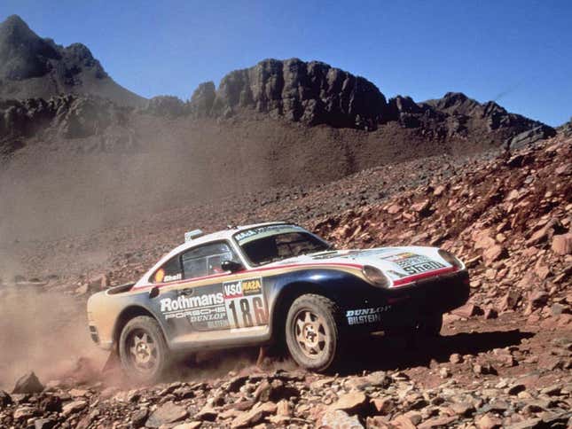 The 1986 Porsche 959 Paris Dakar racecar traverses a rough, boulder-strewn landscape.