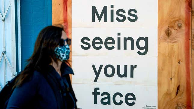 A woman in a face mask walks by a sign posted on a boarded up restaurant in San Francisco, California on April, 1, 2020