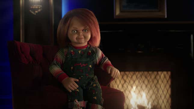 Chucky, killer doll, sits in front of a cozy fire