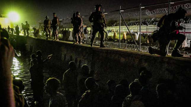 British and Canadian soldiers stand guard near a canal as Afghans wait outside the foreign military-controlled part of the airport in Kabul on August 22, 2021.