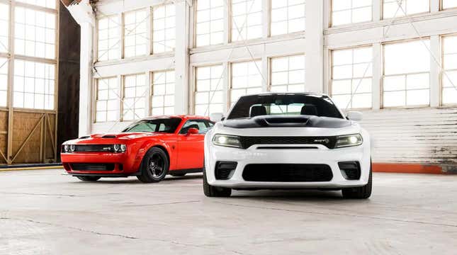 A red Dodge Charger and a white Dodge Challenger sit parked in a white-washed warehouse.
