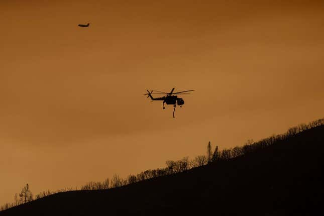 A firefighting aircraft fly through a smoke-filled sky near a burned ridge at the Oak Fire near Mariposa, California, on July 24, 2022.