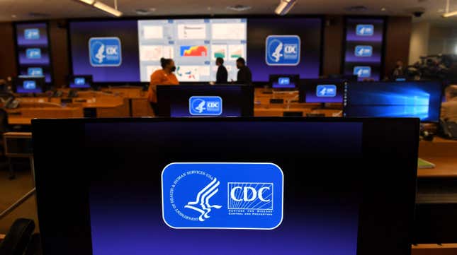 A blue CDC logo is shown on a computer in an emergency center. Other logos can be seen in the background.