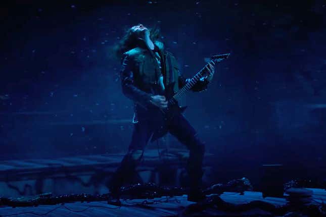 Eddie Munson shreds on his electric guitar in front of an ominously dark sky.