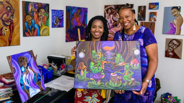Artist Sharika Mahdi and lead Imagineer Charita Carter hold art of frogs in the bayou.