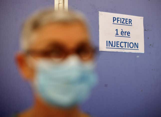 A woman wearing a protective face mask stands by a sign reading "Pfizer first injection" in a vaccination center in Antibes as part of the coronavirus disease vaccination campaign in France