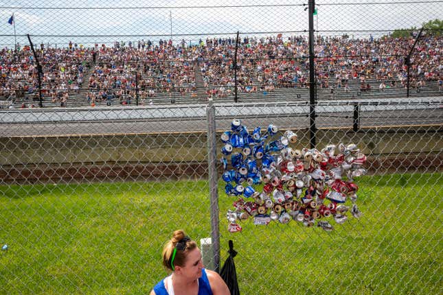 Race fans watch the Indy 500 while simultaneously creating an American flag out of crushed beer cans stuck into a fence