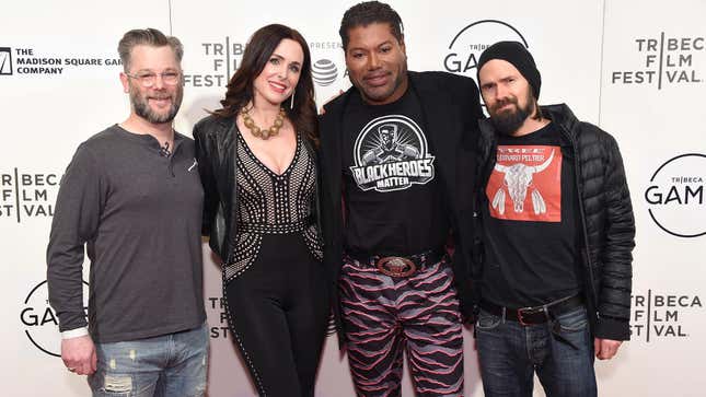 Christopher Judge stands in front of a backdrop for the Tribeca Film Festival with his arms draped over the shoulders of God of War director Cory Balrog and his fellow God of War actors Jeremy Davies and Danielle Bisutti.