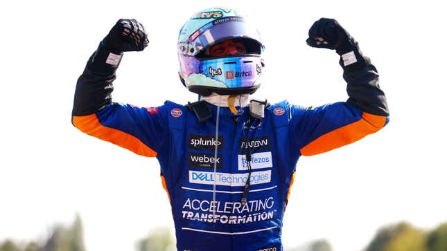 Daniel Ricciardo with his hands in the air in McLaren overalls.