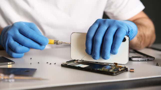 A technician wearing blue gloves using a precision screwdriver to open up a white smartphone for repair