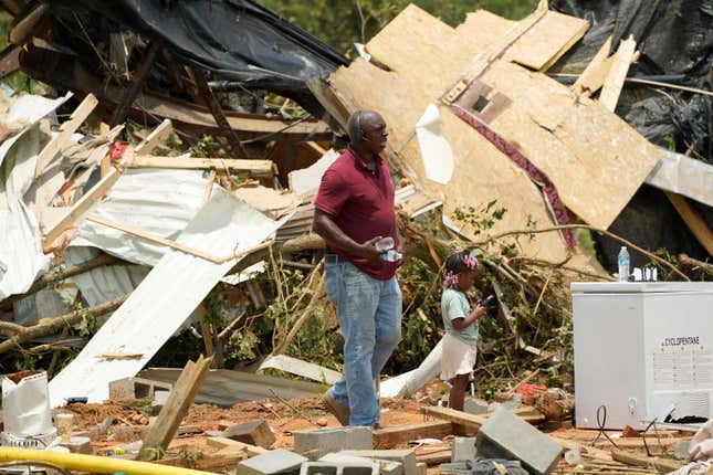 Residents and family members walk past the remains of a mobile home following an overnight tornado that swept through Louin, Mississippi on Monday, June 19, 2023. 